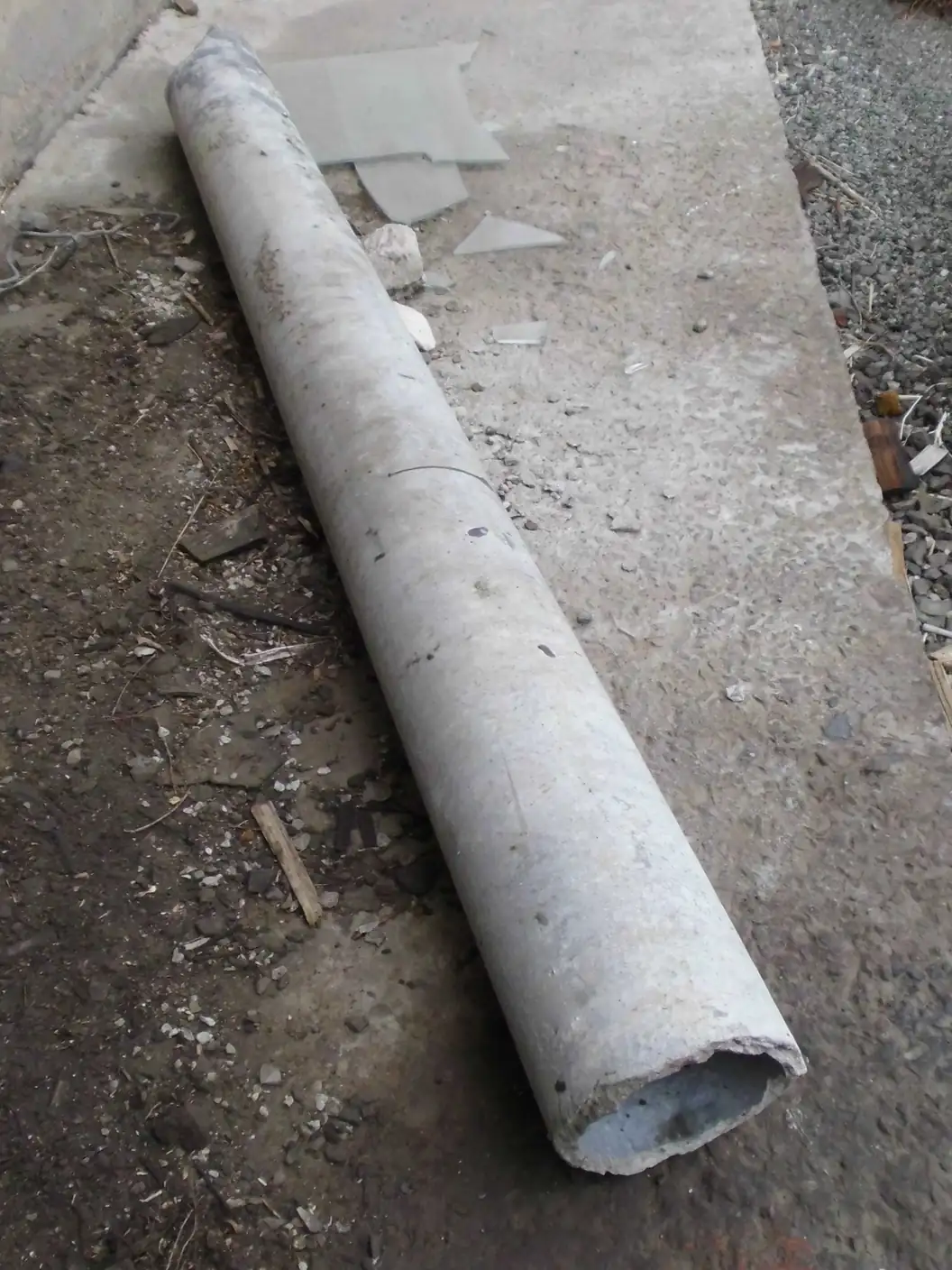 A length of grey asbestos cement pipe lying on a concrete slab, its broken end showing a thick cementitious wall