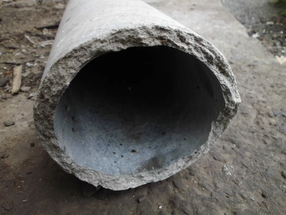 Close view of the broken end of an asbestos cement pipe, a rough grey fracture face around the full wall thickness