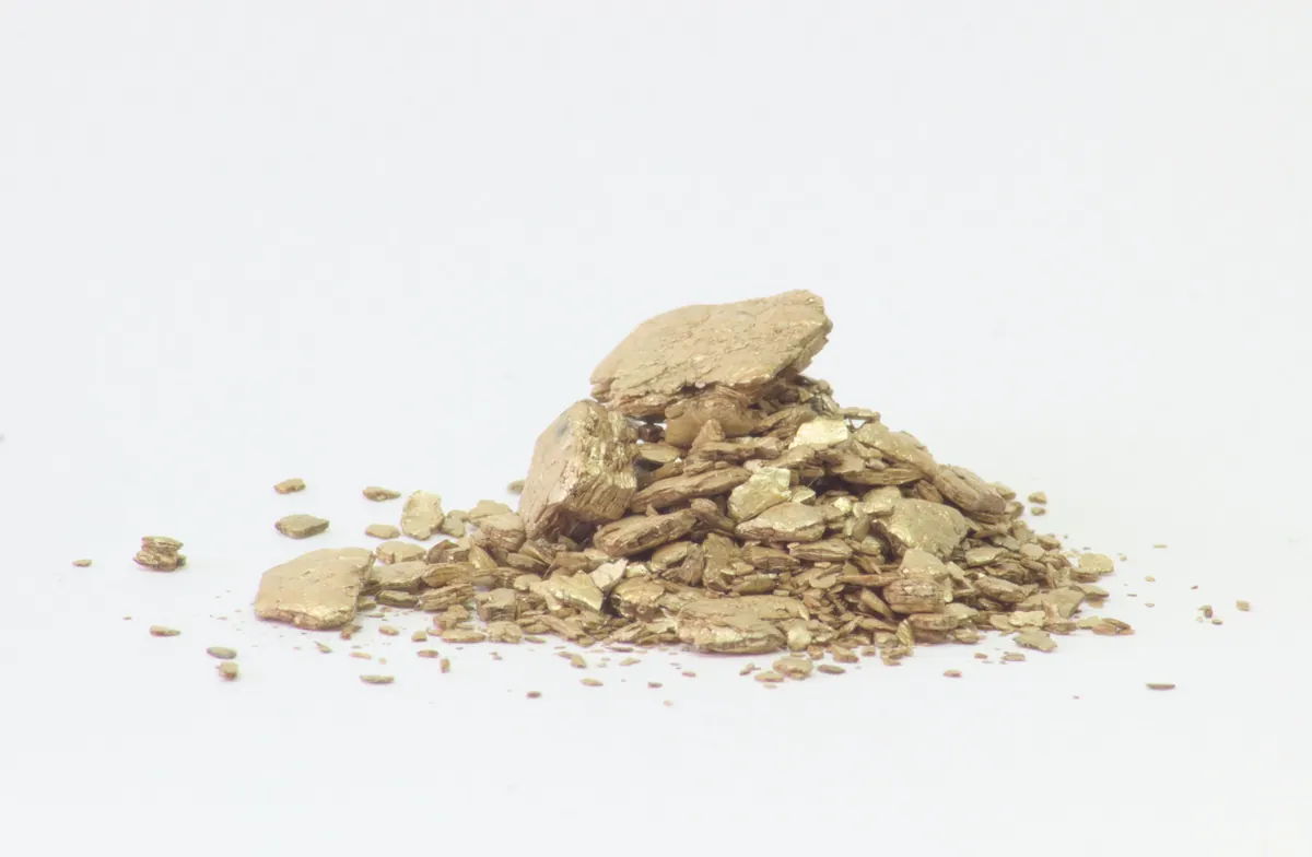 A small heap of expanded vermiculite, golden-brown accordion shaped granules, on a white background