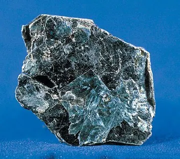 A dark, shiny, mica-like specimen of raw vermiculite on a blue background