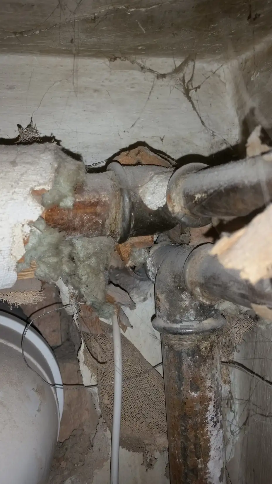 Damaged pipe insulation in a basement with its jacket torn, exposing white and brown fibrous material