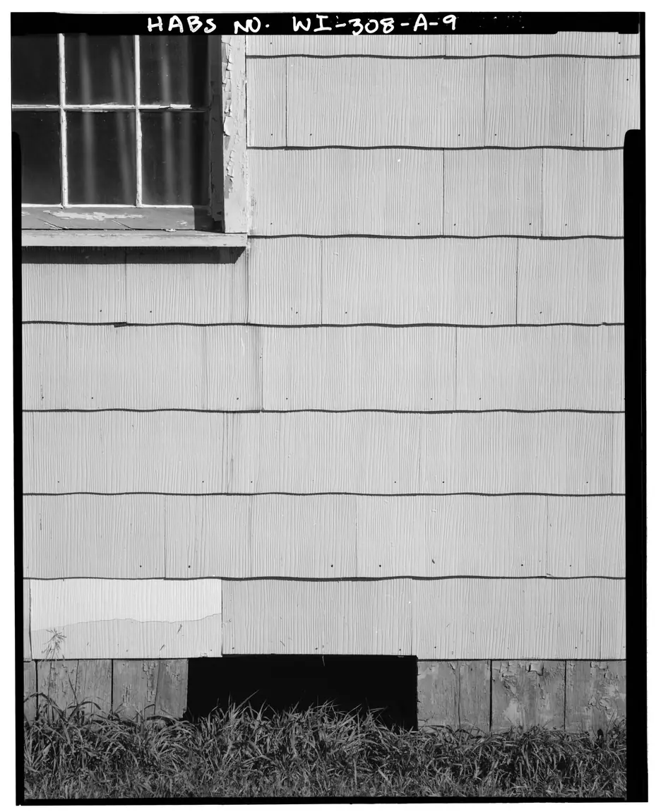 Close view of cement-asbestos siding shingles with a pressed wood-grain face, wavy lower edges and a row of nails near the bottom of each course.