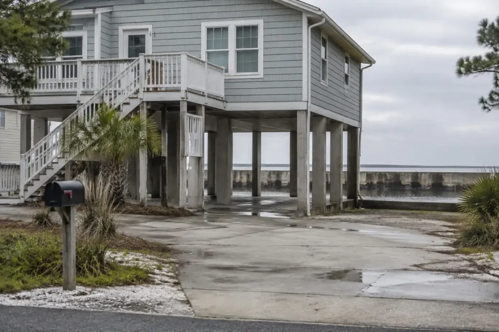 Illustration: a raised coastal house on pilings beside a seawall.