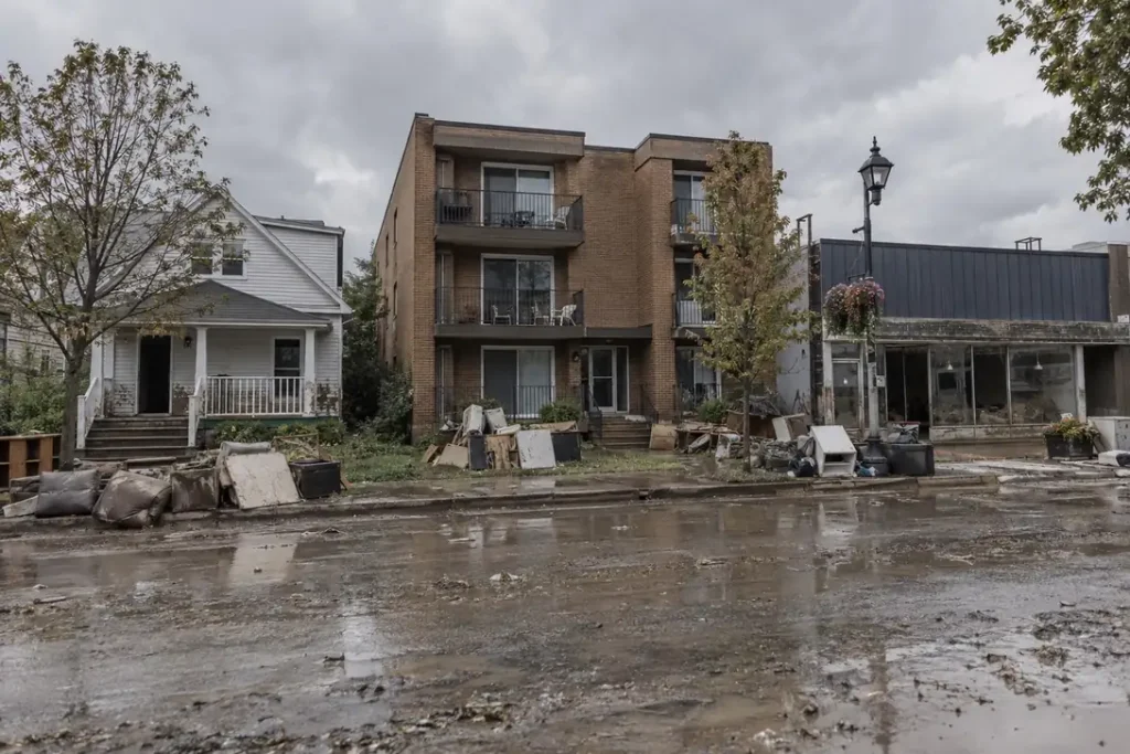 Illustration: a street of mixed residential and commercial buildings after flooding, with debris at the kerb.