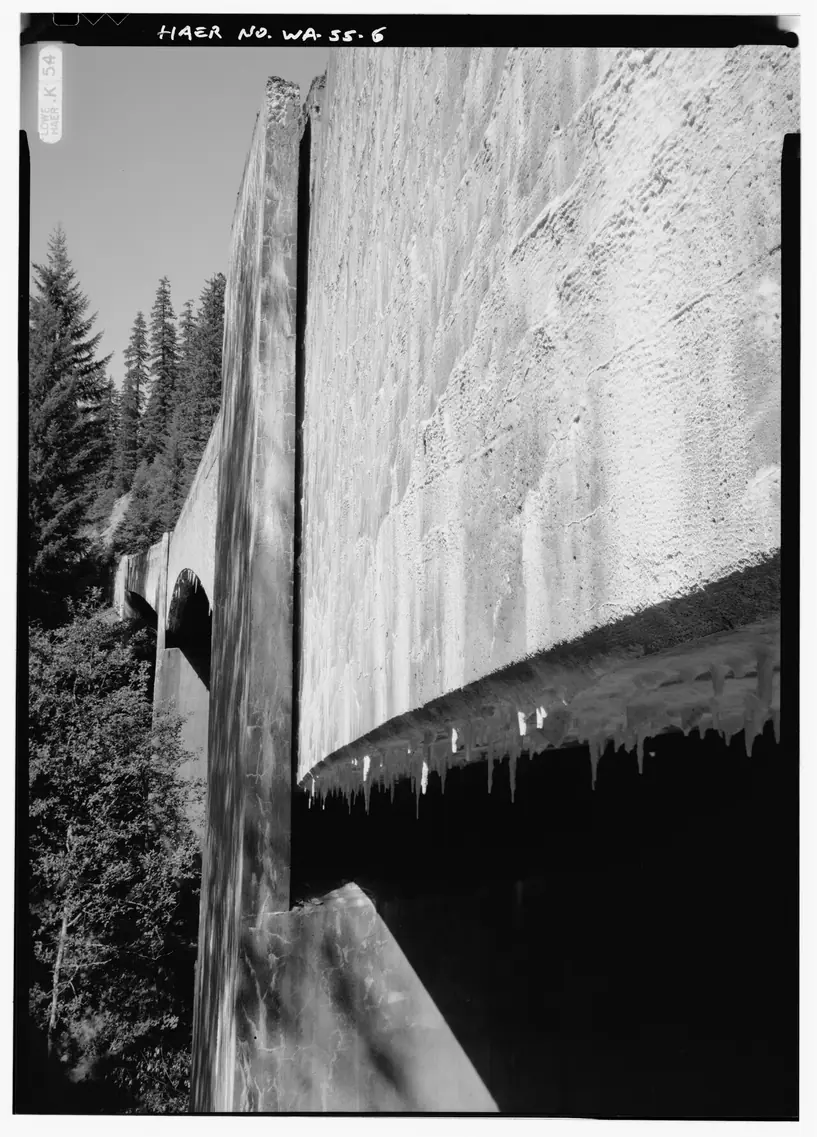 Black and white photo of a concrete bridge girder with white mineral deposits streaking down its face and hanging in drips from its lower edge