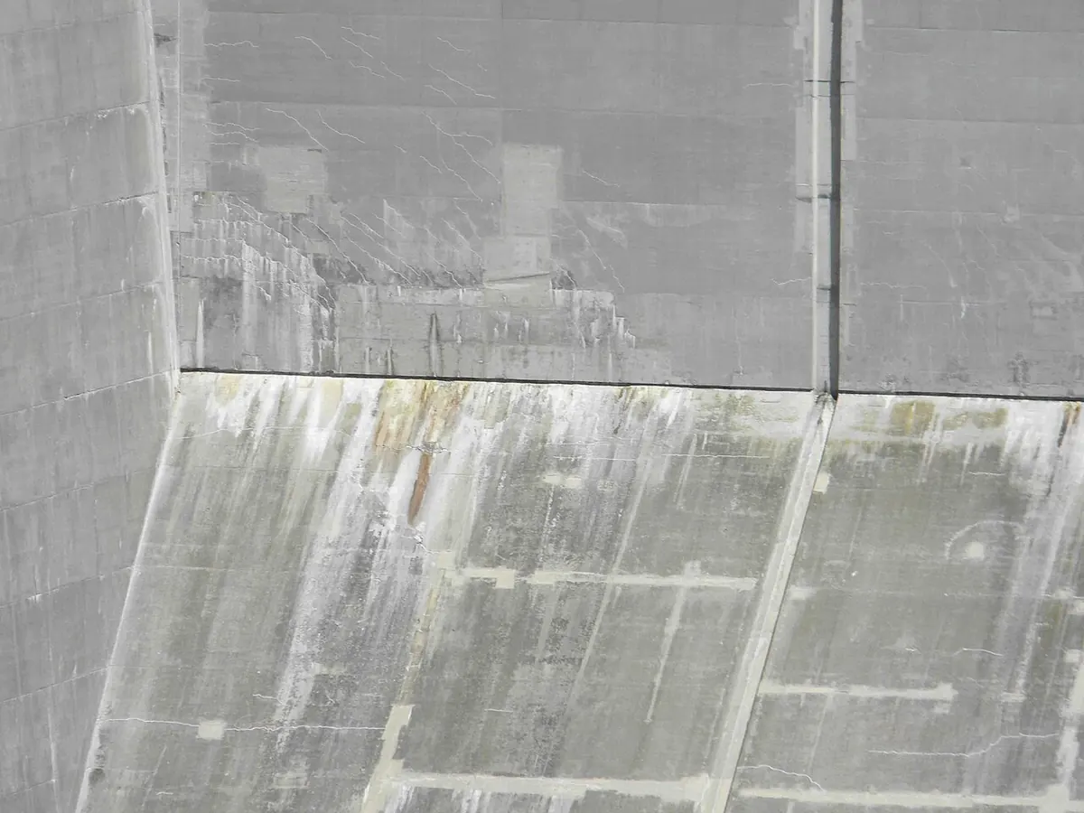 Large concrete wall with white vertical streaks of mineral deposit running down from a horizontal joint