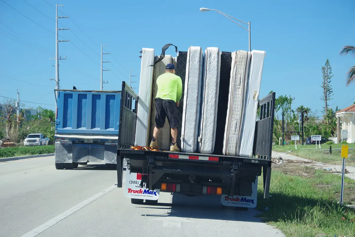 A worker standing on a flatbed truck loaded with upright water-damaged mattresses and box springs on a roadside in Marathon, Florida