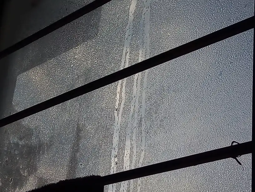 Interior condensation covering window glass in fine droplets, with streaks where drops have run down toward the frame