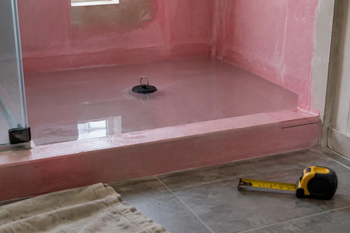 Illustration: a shower floor flood test with a plugged drain and a marked water line on the curb.