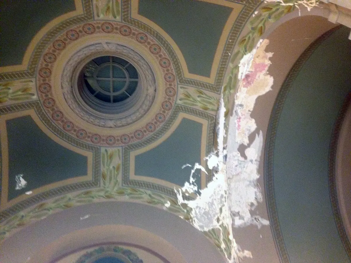 Painted decorative plaster on an arched surface with paint and finish coat flaking away in a long band where water reached it