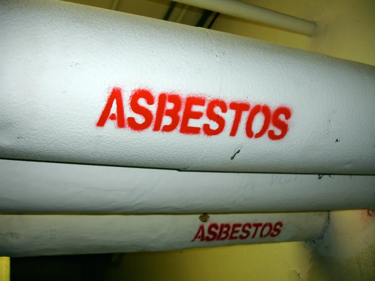 Insulated pipes in a university service corridor stencilled with the word asbestos in red