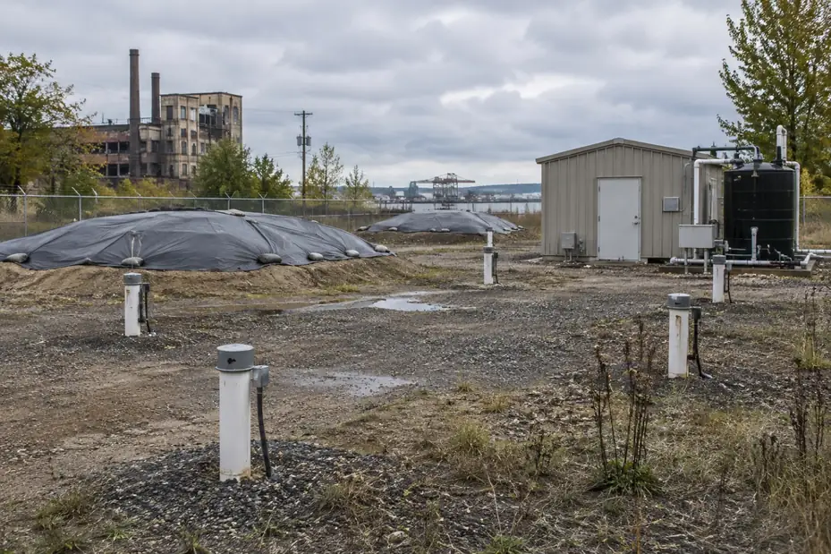 Illustration: an environmental remediation site with monitoring wells and capped soil